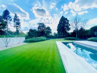 Produktbild von Kiepenkerl Golfrasen Masters Nachsaat tiefschnittverträglich zeigt gepflegten Rasen, Pool und Bäume im Hintergrund